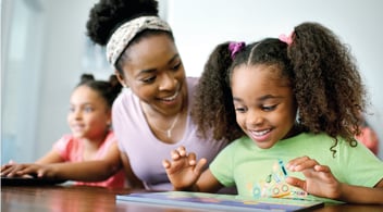 Parent looks on as child happily works on iPad screen